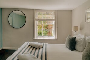 A bedroom with a bed, a window with blinds, a round mirror, and a bedside lamp. - The Ram Inn (Lewes)