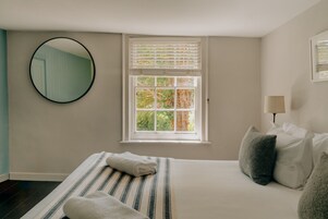 Un dormitorio con cama, ventana con persianas, espejo redondo y lámpara de noche.
