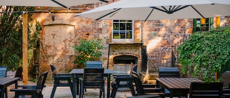 Un patio exterior con paredes de ladrillo, una chimenea y mesas con sillas.