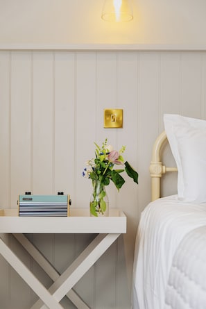 A neatly arranged hotel room with a bedside table, a radio, a vase with flowers, and a bed with white bedding.