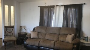 Una sala de estar con un sofá de cuero marrón, una silla de madera, una mesita y un ventilador de techo.