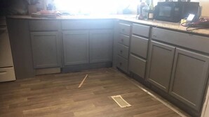 Una cocina con armarios grises, piso de madera y un microondas sobre la encimera.