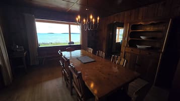 A wooden dining area with a view of the sea, a chandelier, and a wooden cabinet with dishes.