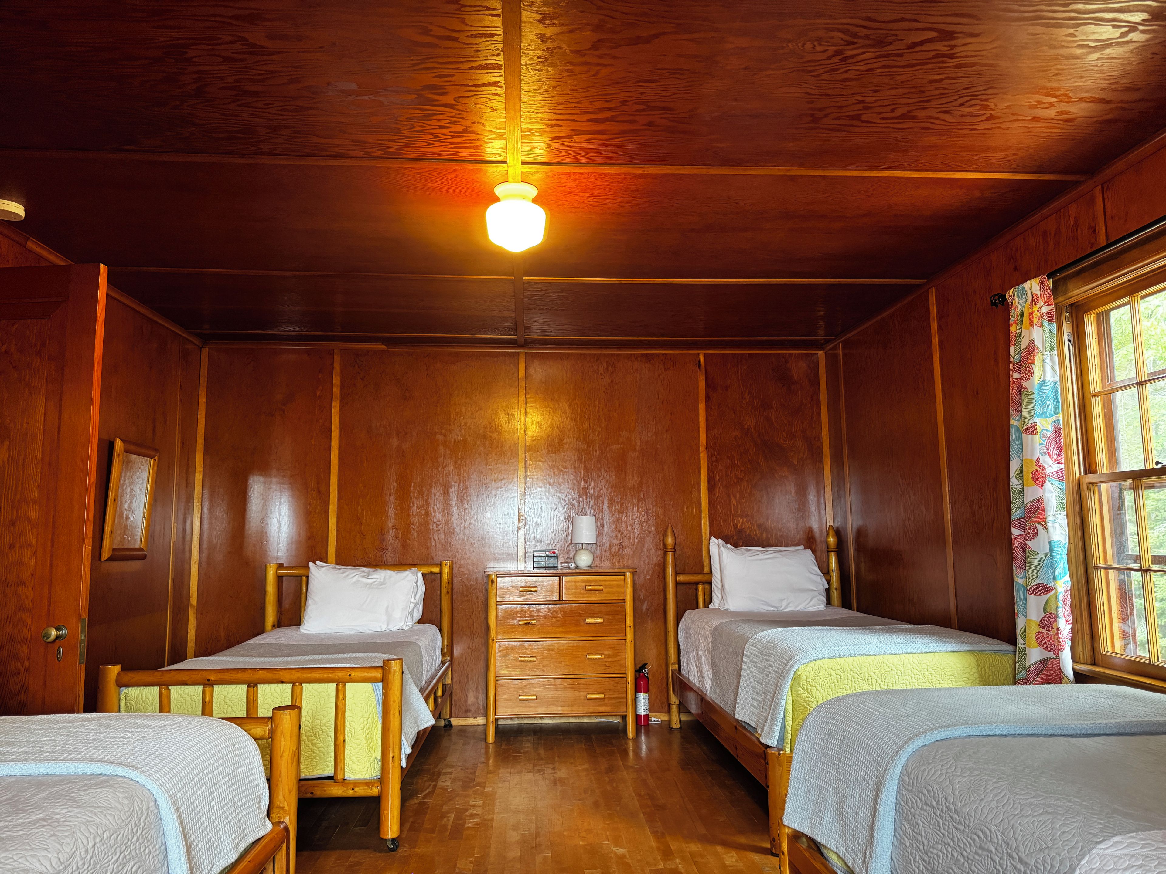 A room with two wooden beds, a nightstand with a lamp, and a window with curtains.