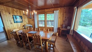Een houten eetkamer met een grote tafel en stoelen, een kroonluchter en een raam met gordijnen.