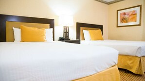 Quarto de hotel com duas camas, cada uma com roupa de cama branca e almofadas amarelas. Há uma mesinha de cabeceira com abajur e telefone entre as camas.