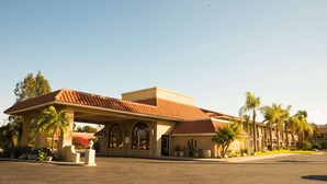 Um hotel com telhado de ladrilho vermelho, entrada coberta e palmeiras por perto.