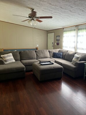 A living room with a sectional sofa, a ceiling fan, and a wooden floor.