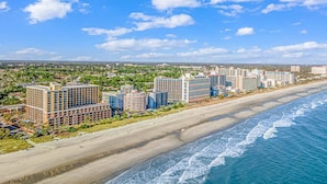 Ein Küstenhotelgebiet mit mehreren Hochhäusern, einem Sandstrand und Blick auf den Ozean.