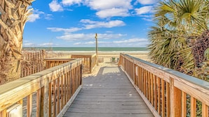 Ein Holzsteg führt zu einem Strand unter blauem Himmel.