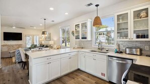 A modern kitchen with white cabinetry, a large island, stainless steel appliances, and a dining area with a sofa and chairs. - Seas The Moment- Pool- Bikes- Golf Cart- Dog Frien (Santa Rosa Beach)