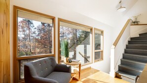 A modern interior with large windows, a staircase, and a wooden floor. - Holiday Hills Escape | Fire Pit | AC | Mt. Holiday (Traverse City)