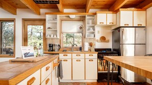 A modern kitchen with wooden cabinets, a stainless steel refrigerator, and a large window. - Holiday Hills Escape | Fire Pit | AC | Mt. Holiday (Traverse City)