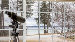 Un telescopio sobre un trípode junto a una ventana con vistas a un lago y árboles.