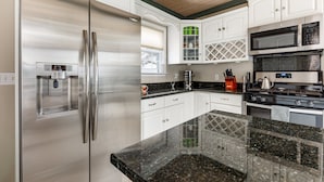Una cocina moderna con electrodomésticos de acero inoxidable, armarios blancos, encimeras de granito y techo de madera.