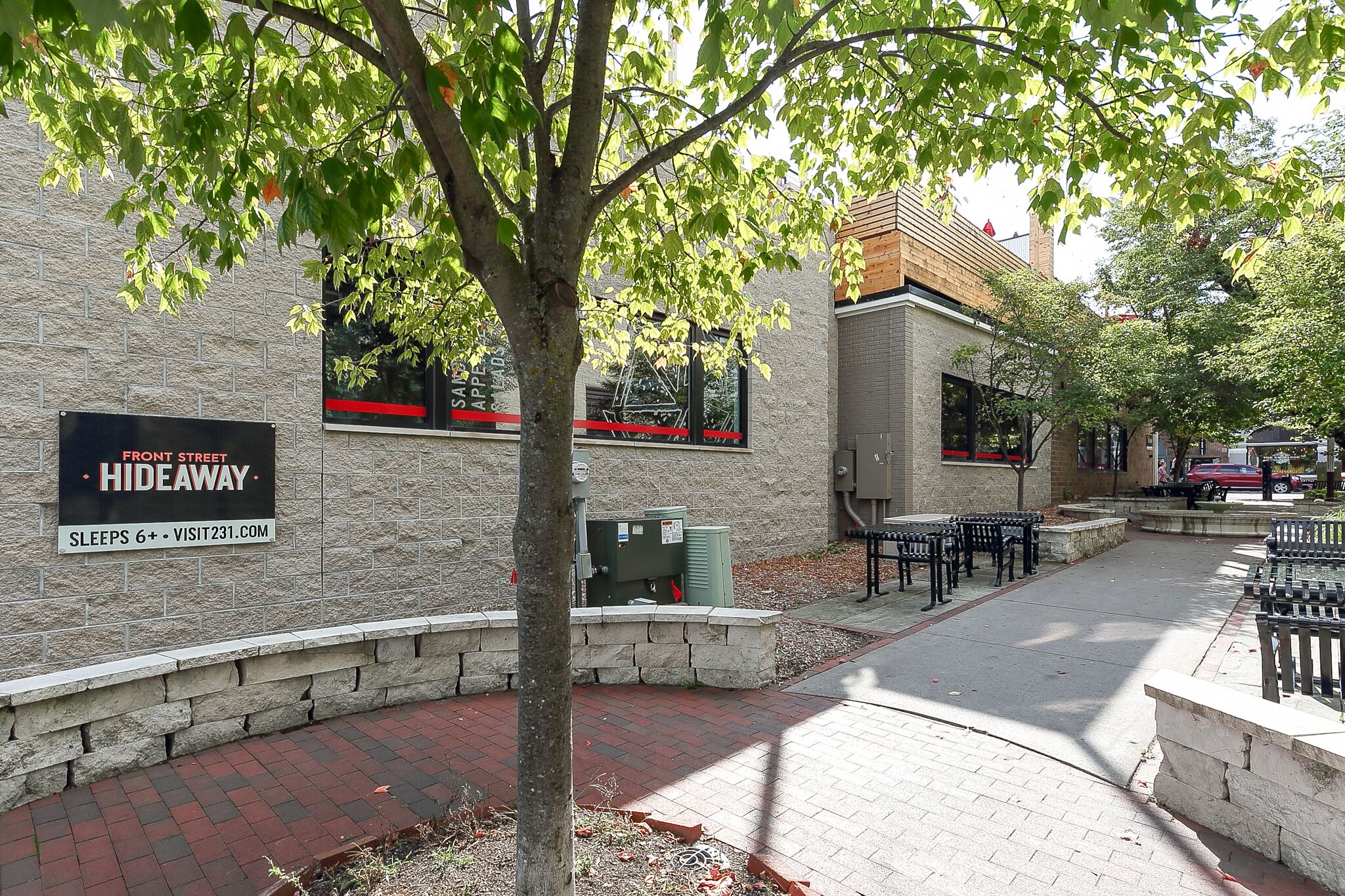 A brick building with a sign indicating it is a Front Street Hideaway. There are benches and a paved walkway.