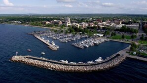 Vista aérea de un puerto deportivo con barcos amarrados, un rompeolas y edificios circundantes.