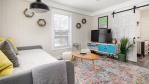 A modern living room with a sofa, a coffee table, a TV, and a sliding barn door. - Contemporary Mid-Century Style | Downtown | AC | (Traverse City)