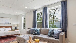 A modern living room with a bed, a sofa, a coffee table, and a window with curtains. - Juniper @ Timberline Flats​​​​​​​ (Traverse City)