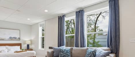 Una sala moderna con cama, sofá, una mesita de centro y una ventana con cortinas.