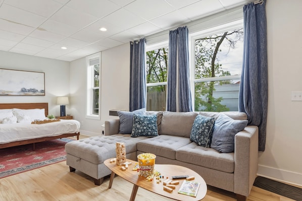 A modern living room with a bed, a sofa, a coffee table, and a window with curtains.