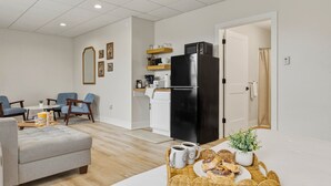 A modern kitchen with a black refrigerator, a dining area with blue chairs, and a living space with a grey sofa. - Juniper @ Timberline Flats​​​​​​​ (Traverse City)