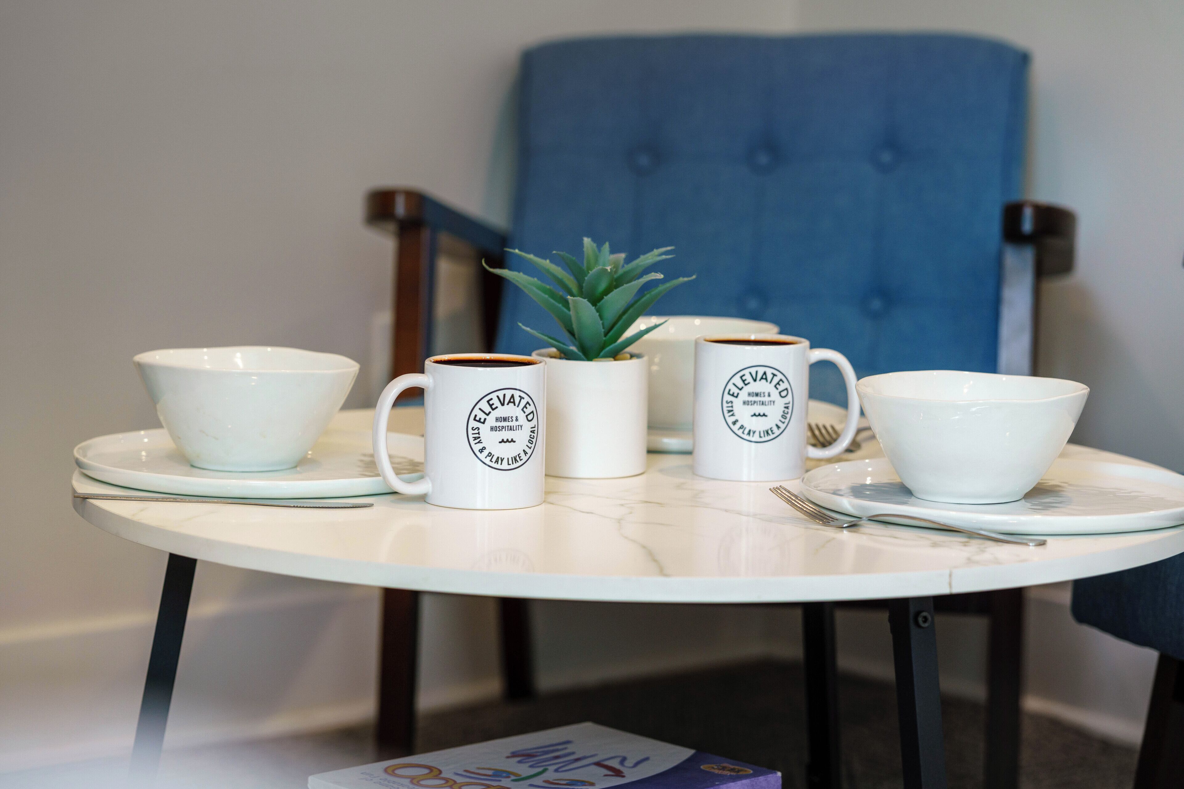 A table with four white mugs, a small potted plant, and a bowl.