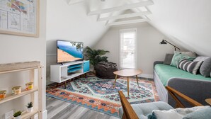 A cozy attic room with a TV, a sofa, a small table, and a patterned rug. - Modern Mid-Century | Downtown | AC | Walkable | (Traverse City)