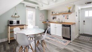 A modern kitchen with white cabinets, a wooden countertop, and a built-in dishwasher. There is a dining table with chairs and a hanging plant. - Modern Mid-Century | Downtown | AC | Walkable | (Traverse City)