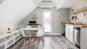 A modern kitchen with white cabinetry, a dining area with a round table and white chairs, and a small island with a plant. - Modern Mid-Century | Downtown | AC | Walkable | (Traverse City)