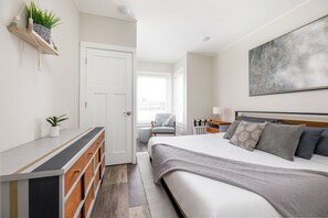 Une chambre à coucher comprenant un lit, des tables de chevet, une commode, une chaise et un grand tableau abstrait accroché au mur.
