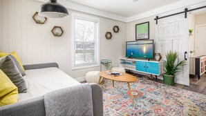 Un salon moderne avec un canapé, une table basse, un téléviseur et un tapis coloré.