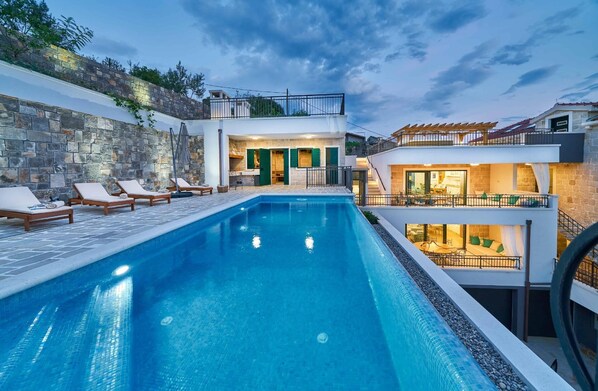 Relax by the pool with lounge chairs and a sunshade, surrounded by a stone wall and a wooden balcony.