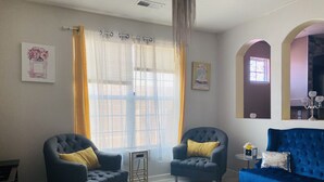 Uma sala de estar com duas poltronas, um sofá azul, um tapete estampado e uma janela com cortinas.