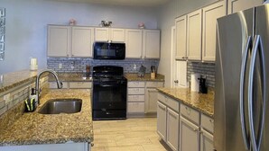 Uma cozinha moderna com bancadas de granito, eletrodomésticos de aço inoxidável e armários brancos.