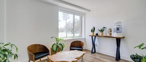 A room with a wooden floor, a table with a leather-like top, two chairs, a window, and a water dispenser.