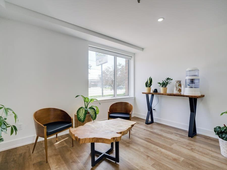 Una habitación con piso de madera, una mesa con cubierta similar a cuero, dos sillas, una ventana y un dispensador de agua.