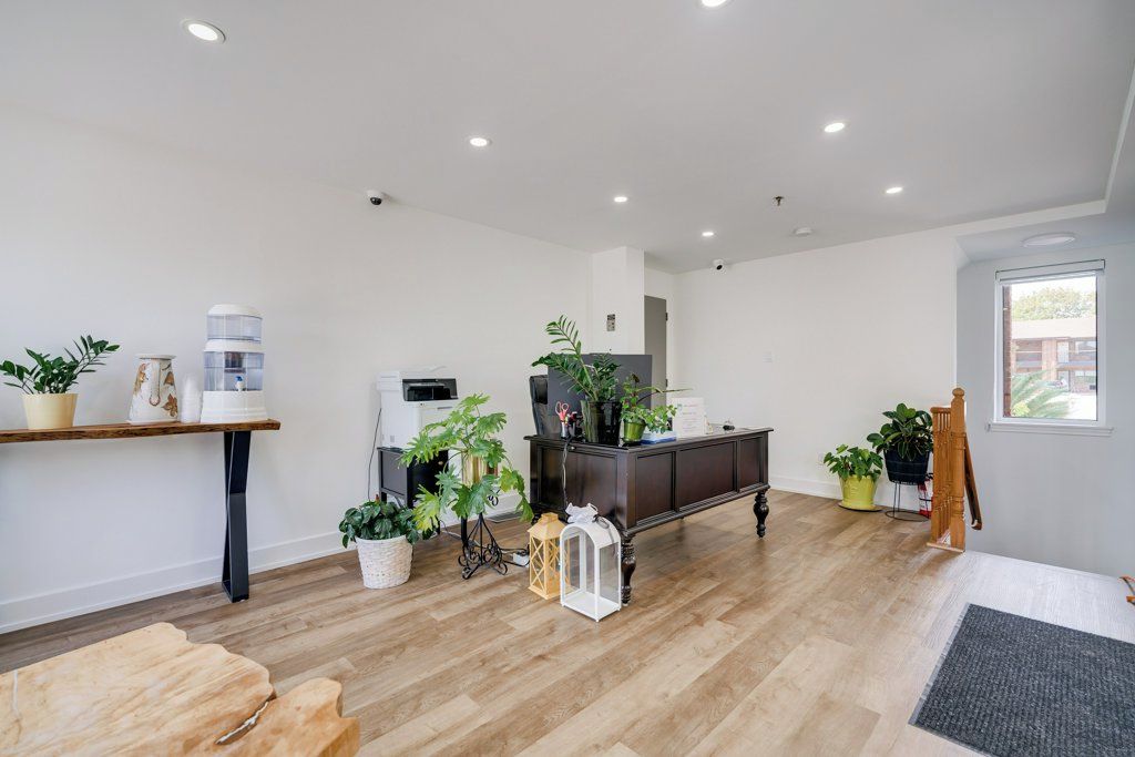 A spacious living area with a wooden floor, a dark-colored cabinet, and several potted plants.