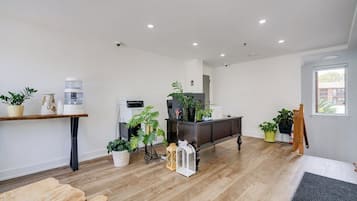 A spacious living area with a wooden floor, a dark-colored cabinet, and several potted plants.