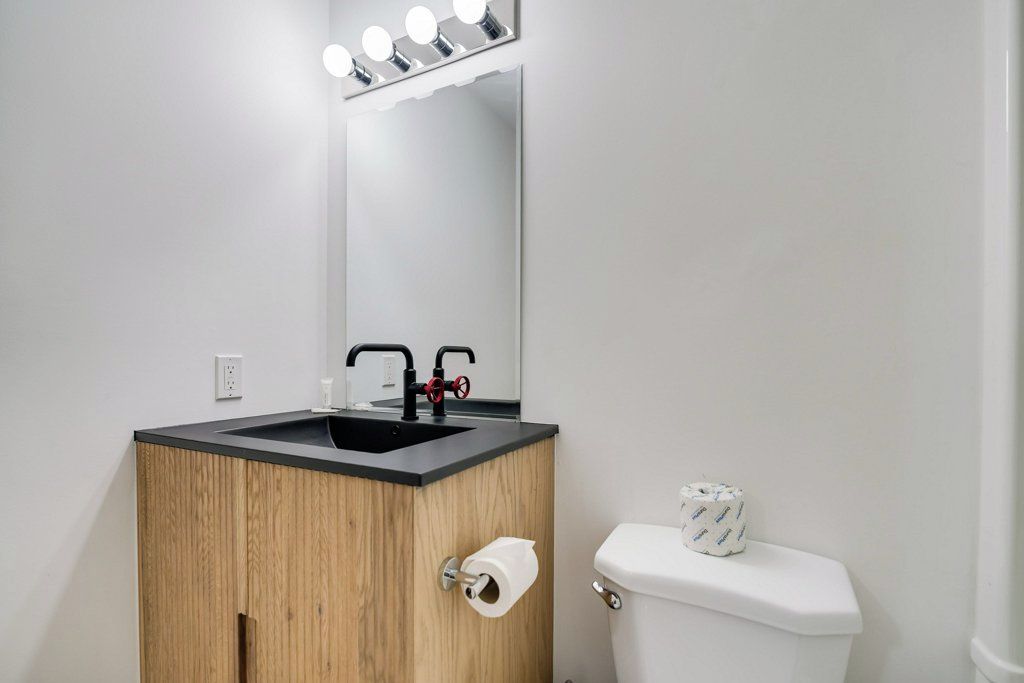 Un bagno con un mobile bagno in legno, un lavabo nero, uno specchio con illuminazione, un water e un rotolo di carta igienica.