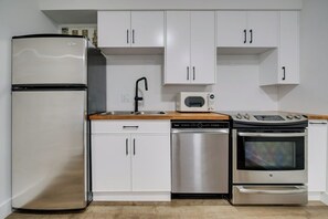 A compact kitchen with white cabinets, a stainless steel refrigerator, a dishwasher, a microwave, and an oven. - Toronto Lakeshore Hotel (Mississauga)