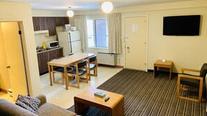 Une chambre d’hôtel compacte comprenant un coin cuisine, un espace repas, un salon avec un canapé et une table basse, ainsi qu’un téléviseur fixé au mur.