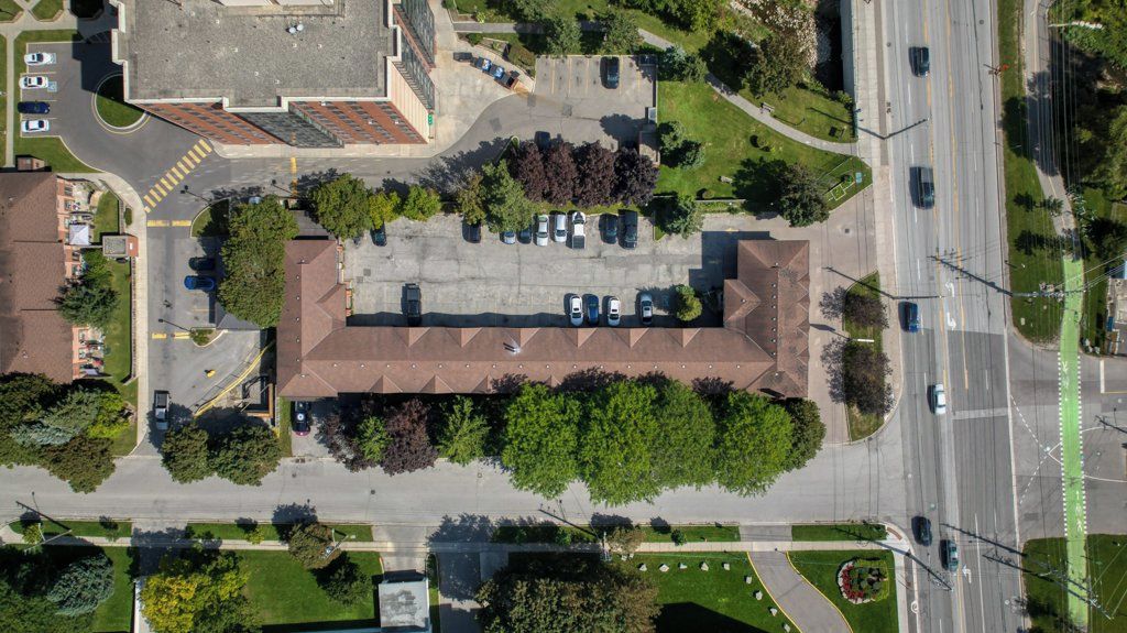 An aerial view of a building with a parking lot, surrounded by greenery and a road.