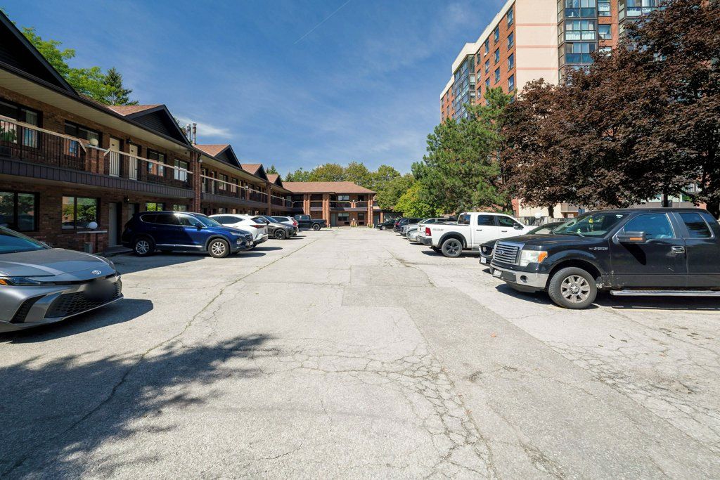 A parking lot with multiple cars, a building with a brick facade, and a taller building in the background.