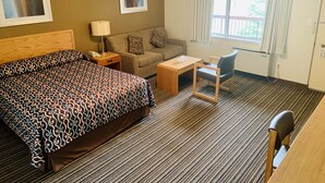 Une chambre d’hôtel avec un lit, un bureau, une chaise, un canapé et une fenêtre avec des rideaux.