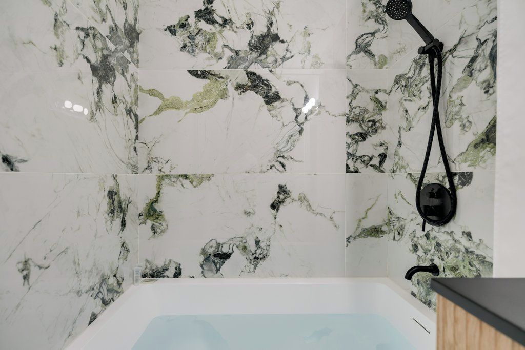 Un baño con pared de mármol, bañera y cabezal de ducha manual.