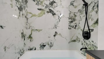 Un baño con pared de mármol, bañera y cabezal de ducha manual.