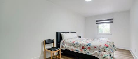 Un dormitorio con cama, una silla, un ventanal y una lámpara de techo.