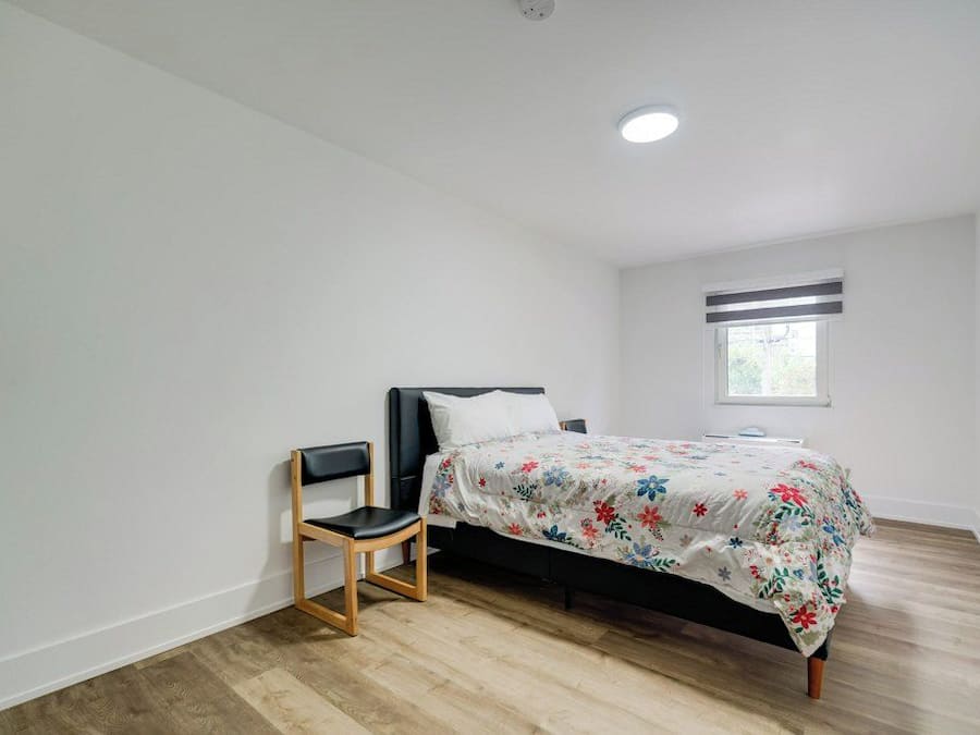 A bedroom with a bed, a chair, a window, and a ceiling light.
