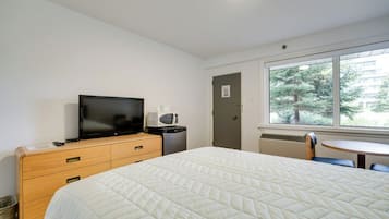 Habitación de hotel con una cama, televisión, microondas, una mesita y ventana con vistas a árboles.